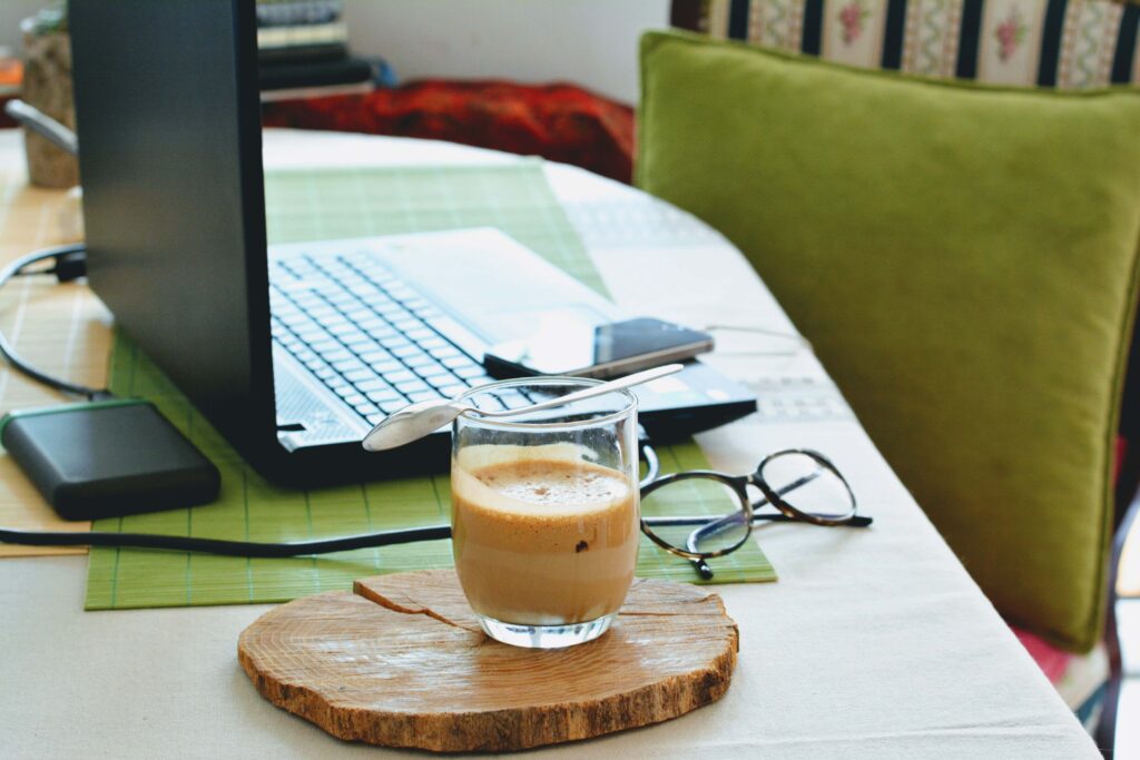 A work from home setup: large table with a laptop, coffee and glasses