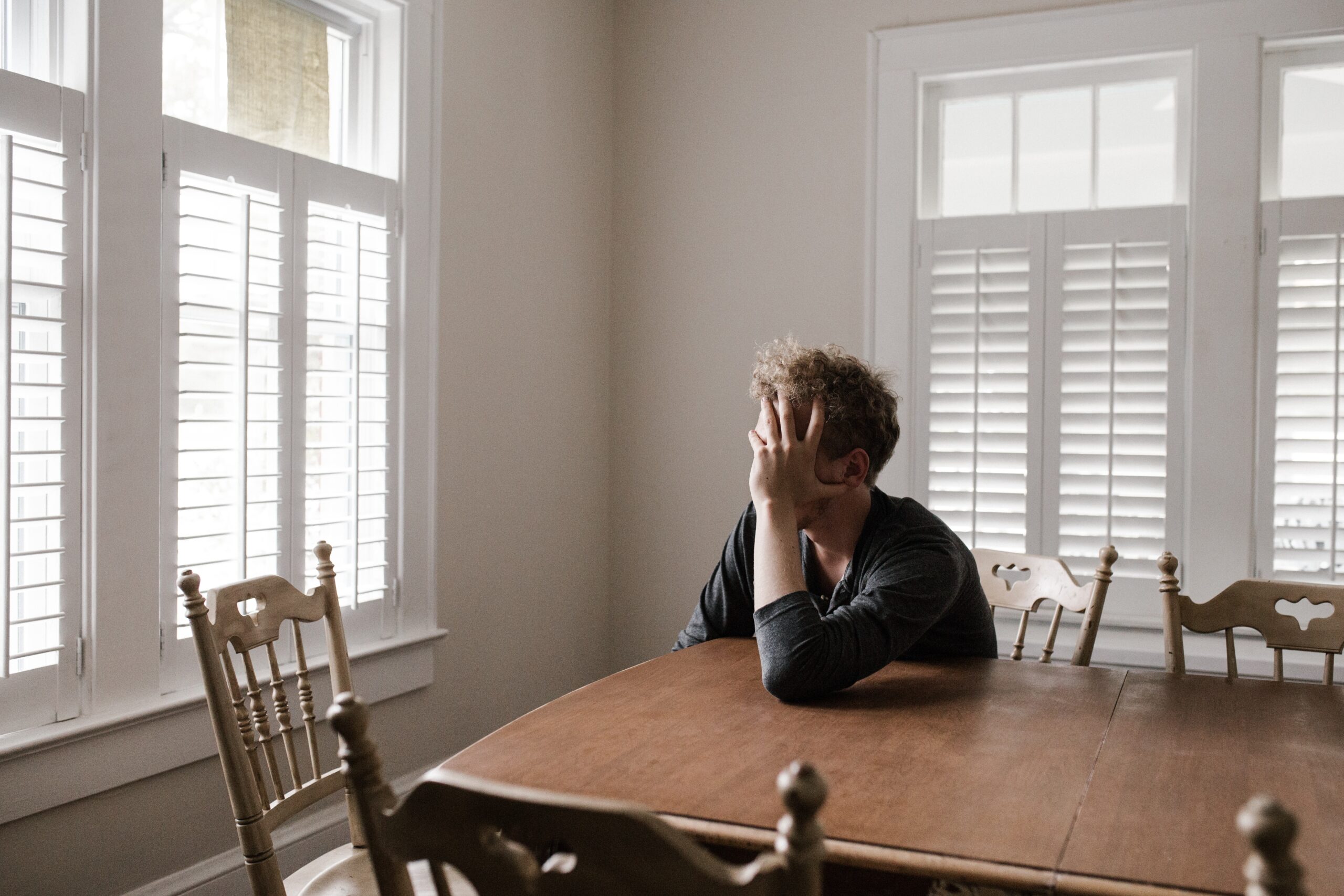 A man sitting at a table holding his head in his hand. Coronavirus layoffs have left many feel a bit desperate.