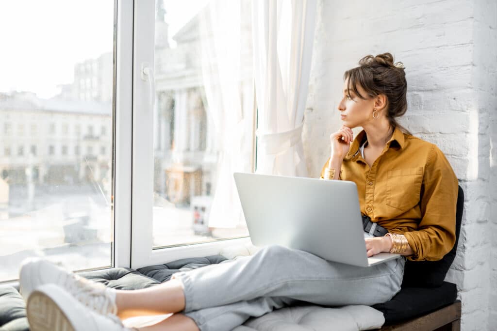 Woman working from home with laptop on the window sill