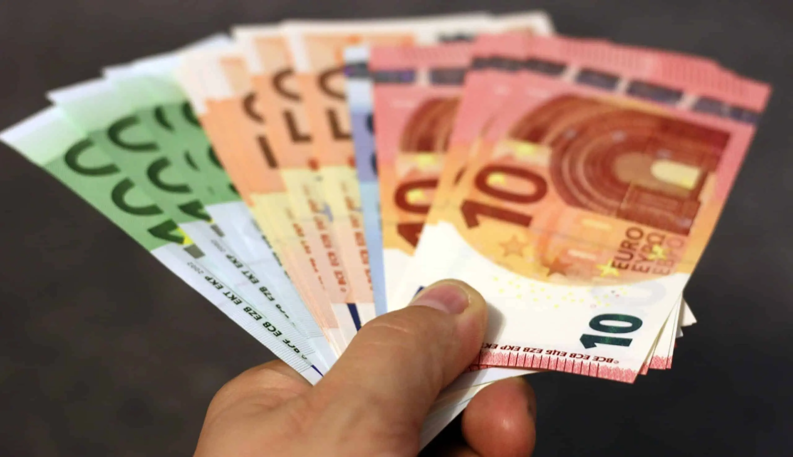 A hand holding a fan of various Euro banknotes on a dark surface.