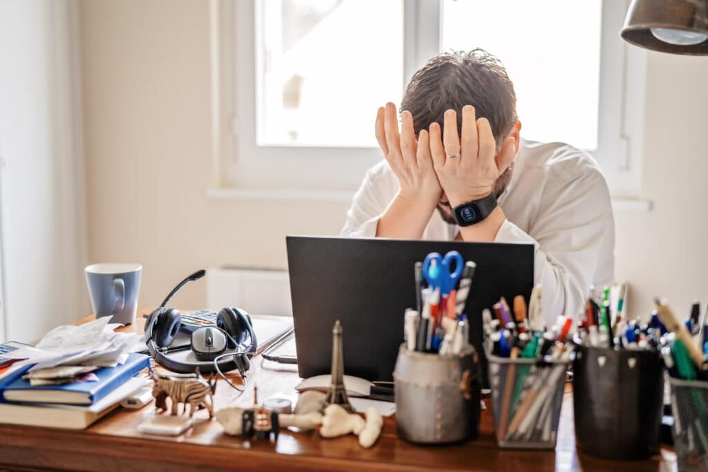 Tired frustrated businessman working from home online sitting at home office with laptop during quarantine and self isolation period at pandemic